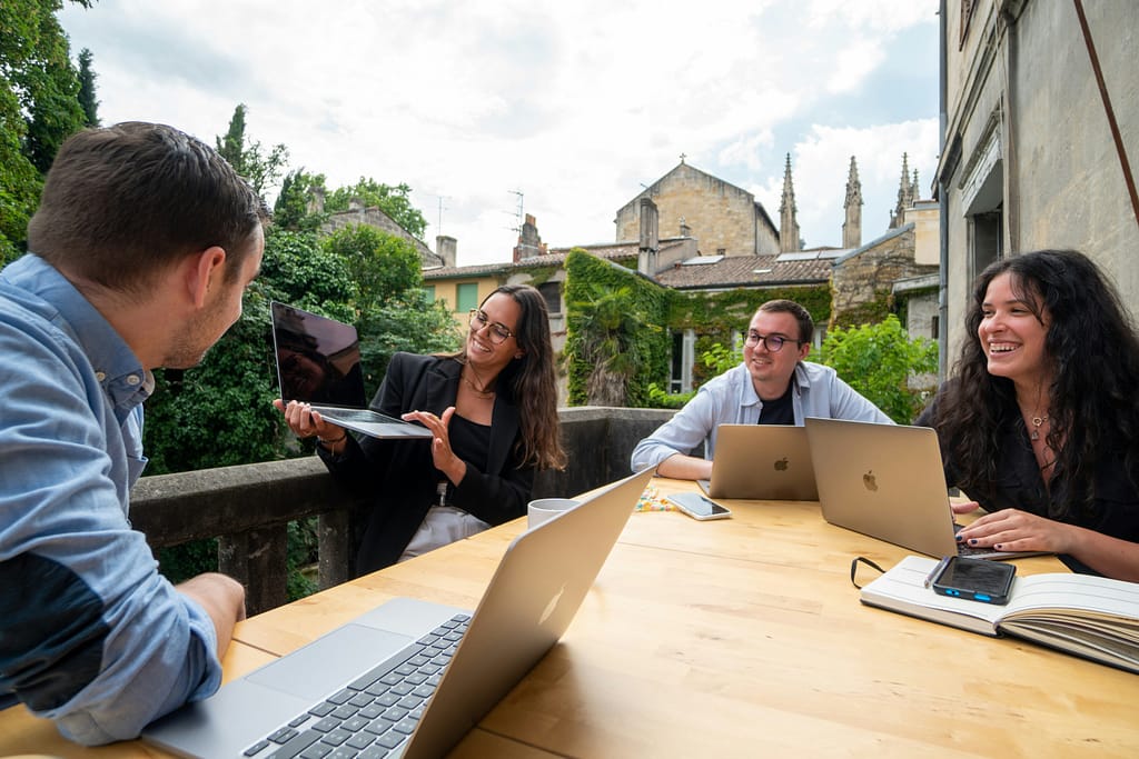 People sitting around a table outside working on laptops